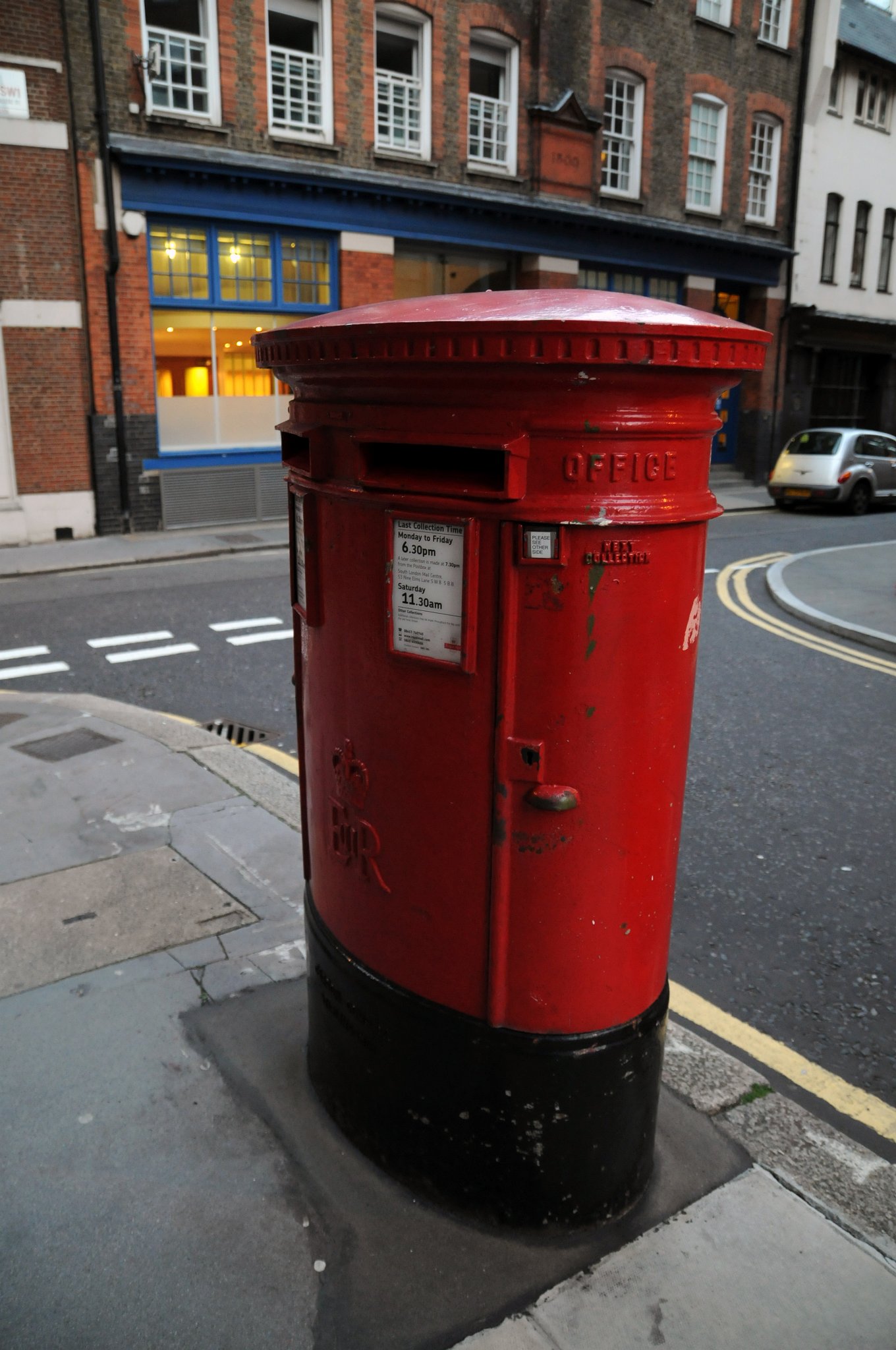 DSC_3465_1.jpg - Tradiční snad až ikonická poštovní schránka v Londýně. Schránky jsou červené od roku 1874, kdy vládla královna Viktorie. První poštovní schránky se v londýnských ulicích objevily v roce 1855. Byly umístěny na Fleet Street, Strandu, Pall Mall a Rutland Gate. Žádná z nich se nezachovala. Nejstarší schránky, které můžeme v britské metropoli najít, jsou z roku 1872. O dva roky později dostaly svou typickou červenou barvu, kterou září dodnes. Původně však byly natřeny na zeleno. Na každé britské poštovní schránce jsou iniciály panovníka, za jehož panování byla vyrobena, tedy královnou Viktorií počínaje a Alžbětou II. konče. Díky těmto litinovým boxům se alespoň něco málo uchovalo i z vlády Edwarda VIII., který abdikoval v roce 1936, ještě před svou korunovací. V Londýně je v současnosti osm velkých sloupových schránek s jeho monogramem.