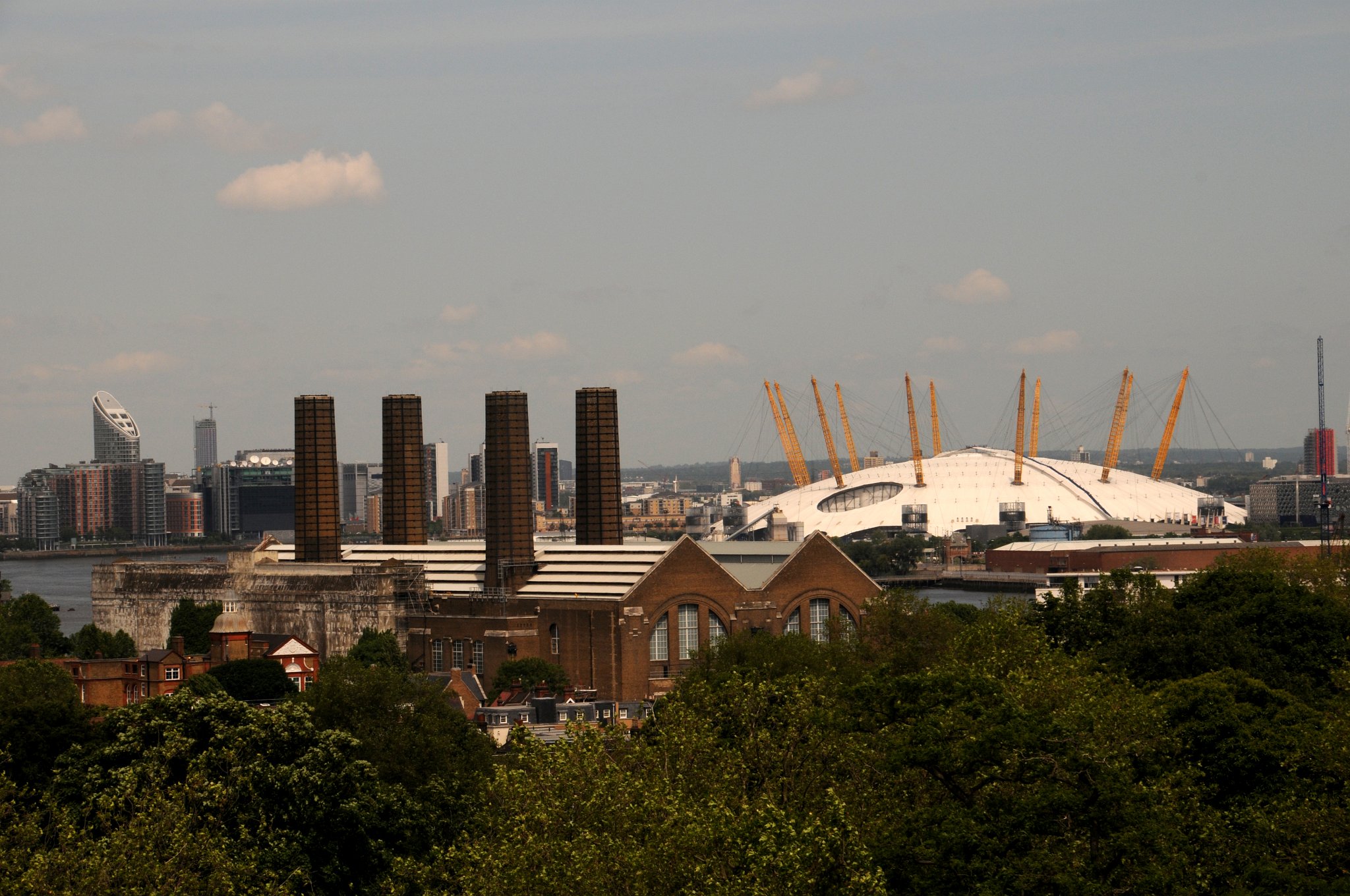 DSC_4063_2.jpg - Pohled z Greenwich na Millennium Dome. Dóm je největší samostatně zastřešenou stavbou světa. Z vnějšku vypadá jako velký bílý kupolovitý stan s dvanácti 95 m vysokými žlutými podpěrnými sloupy. Průměr kruhové stavby je 365 m. Je snadno viditelný na leteckých snímcích Londýna. Tvarem připomíná dóm postavený pro Britský festival roku 1951. Architektem stavby byl Richard Rogers. Materiál střechy je teflon potažený tkaninou ze skleněných vláken. Hmotnost vlastní střechy je menší než hmotnost vzduchu uzavřeného její konstrukcí a ve středu budovy Millennium Dome se střecha vypíná do výšky 50 m. Její plocha je přerušena otvorem, kterým vede ventilace z Blackwallského tunelu. Velvo je pak Greenwich Electric Power Station.