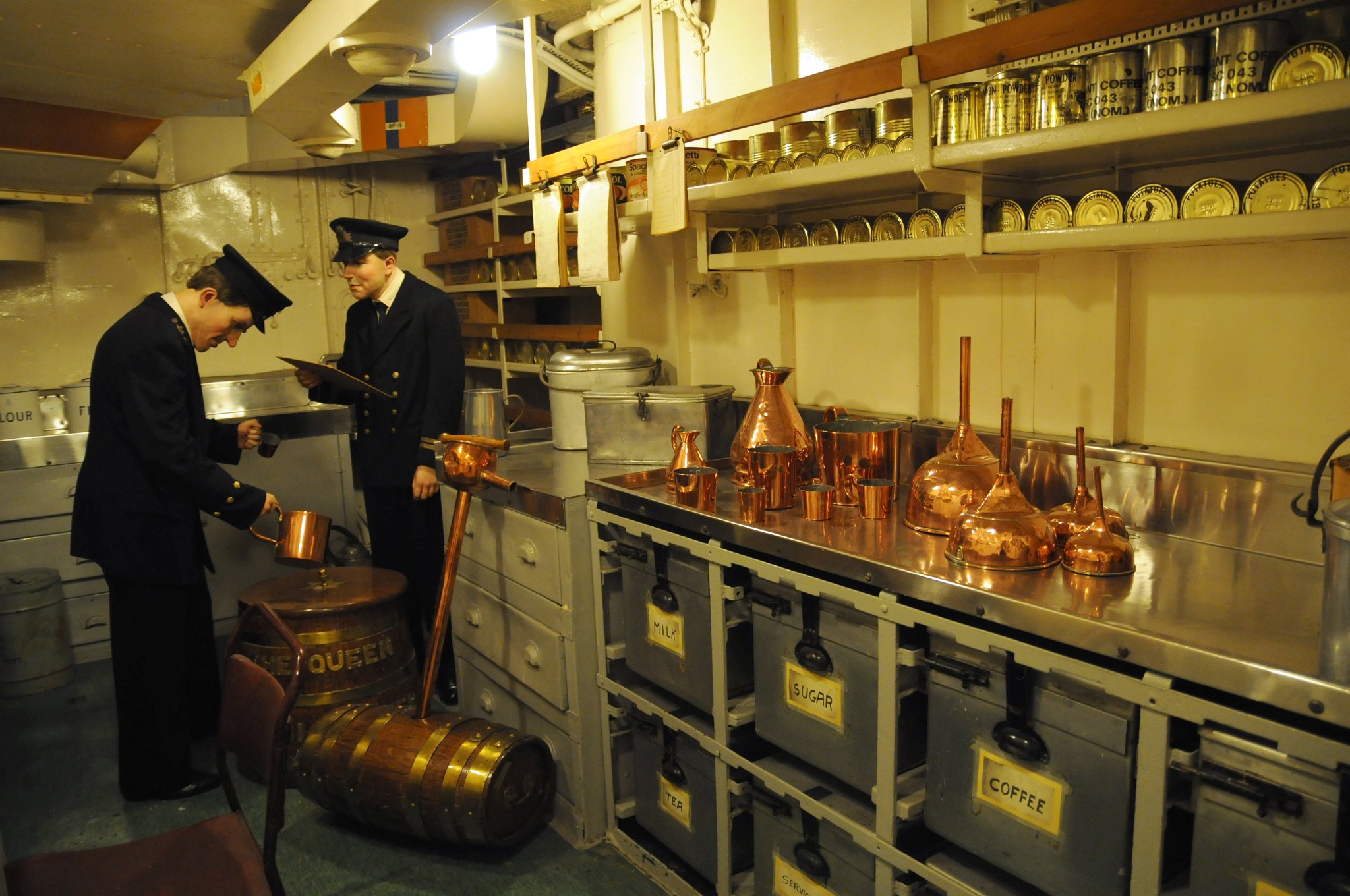 DSC_4817_1.jpg - Distribuce potravin a denní přídely rumu známé jako ´Up Spirits´ byly vydávány zde. Během Korejské války HMS Belfast posádka spotřebovala přes 56 000 pint (32 000 litrů) rumu! Lodní sklad a chladicí prostory se nachází dvě paluby níže. Příděly musely být dodržovány, protože HMS Belfast byl na moři až po dobu tří měsíců. Britští námořníci prý tradičně dostávali denní příděl půl pinty (asi 0,3 l) alkoholu, avšak prý již od 18. století byl zaveden koncept pití grogu. Rum se mužstvu vydával z nádherného dřevěného sudu s nápisem ''Bůh žehnej královně''.