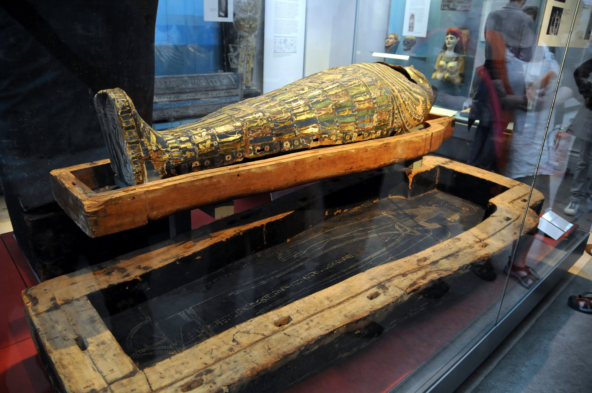 DSC_5880_2.jpg - Mumie kněze Hornedjitefa (3. století př. nl) byla uzavřena v pozlacené lepenkové masce a pláštěm uložena ve dvou do tvaru človeka tvarovaných dřevěných rakvích. Rakve byly zdobeny dle tradičních egyptských pohřebních zvyklostí. Vnitřní rakev má jemné namalovanou pozlacenou tvář s vousy a bohatě zdobeným límcem. Na hrudníku je ozdobou scéna v níž Hornedjitef zbožňuje čtyři božstva. Pod límečkem je obraz Boha Slunce a okřídleného scarab brouka, kterého obklopují paviáni, kteří uctívají rostoucí sluneční ktouč. Pohřební text je zapsán v hieroglyfech níže. Jedna strana textu jsou postavy božstev: čtyři Synové Hora, bohyně Isis a Nephthys.Interiér víka zdobí mnoho postav, většinou týkající se astronomie. Jejich pozice na víku rakve je zvláště vhodná v rámci symboliky nebes táhnoucím nad zesnulým.