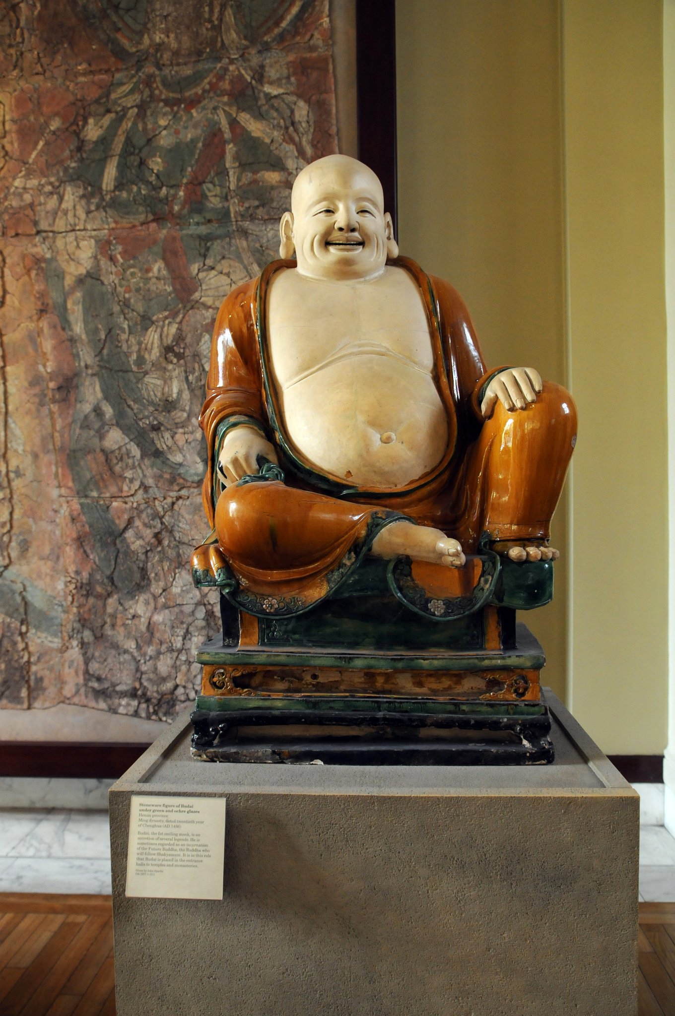 DSC_5955_2.jpg - Kameninová figura Budhy v zelené a okrové glazuře. Henan provincie, Dynastie Ming, 20 léta Chenghua, 1486 našeho letopočtu. Budai, tučný smějící se mnich. několik legend. Někdy je považován za ztělesnění budoucnosti Buddha, Buddha, který bude následovat Šákjamuniho. V této roli je umísťován ve vstupních halách do chrámů a klášterů.