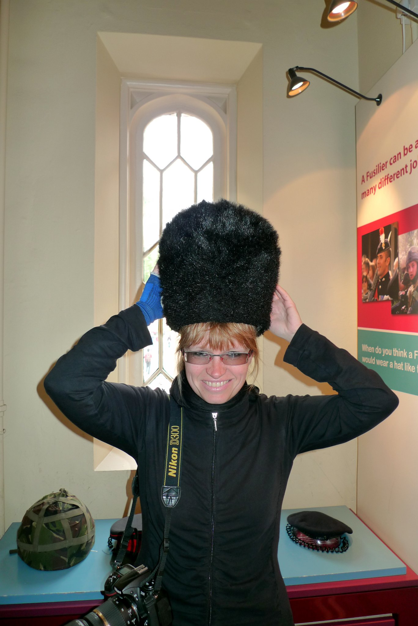 P1070541_1.jpg - V Regimental Museum of the Royal Fusiliers jsem si vyzkoušela, jaké to je mít na hlavě čepici gardy. Chtělo by to ale rozpustit vlasy, culík mi bránil, nasadit ji na hlavu.