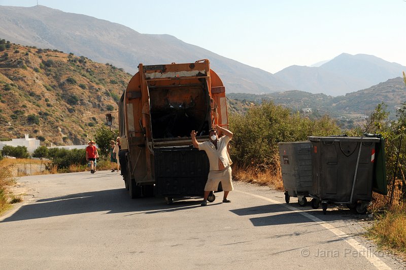 DSC_3093_2.jpg - Na Krétě nemají lidé popelnice. Na kraji vesnice je místo toho obvykle pár kontejnerů, do kterých lidé vhazují své odpadkové pytle. Vzhledem k teplu se vůbec nedivíme tančícímu popeláři, že používá roušku. 
